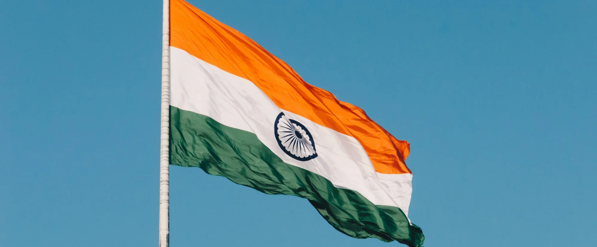 Large Indian flag fluttering in the wind attached to a white flagpole