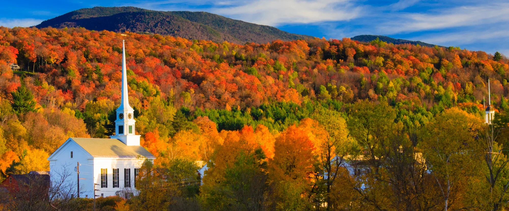 White New England church surrounded by yellow and red autumnal foliage